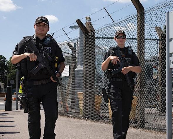 Two police firearms officers walking beside a fenceline