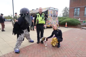 Ian (centre) standing with PD Maddie, and a cheerleader from the Baltimore Ravens and their mascot at RAF Molesworth 
